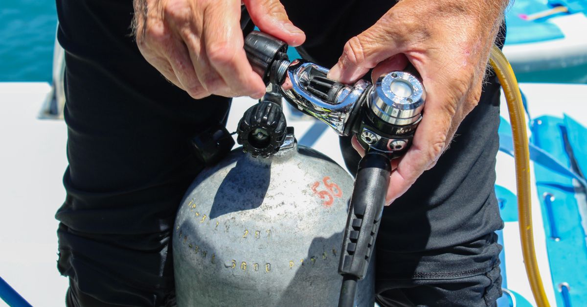 Scuba gear set near a dive boat and tropical shoreline before a dive day.