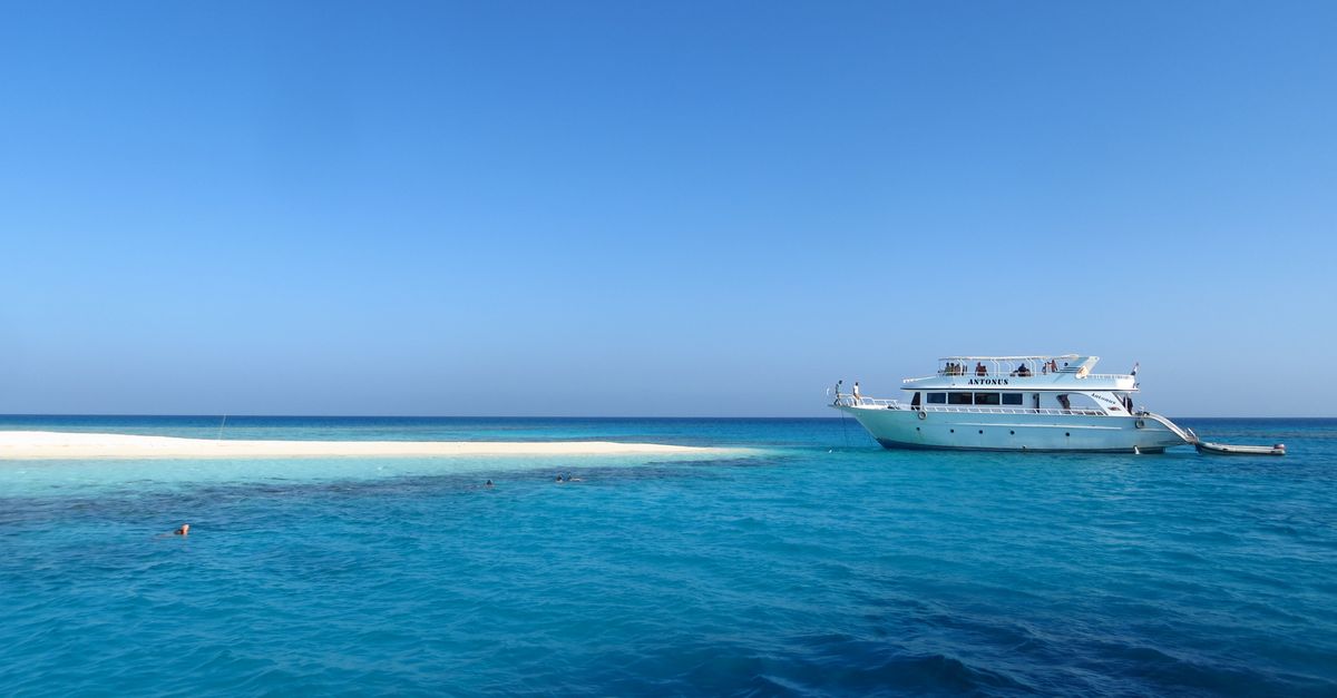 A diver and non-diving travel partner planning a tropical trip near a beach and dive boat.