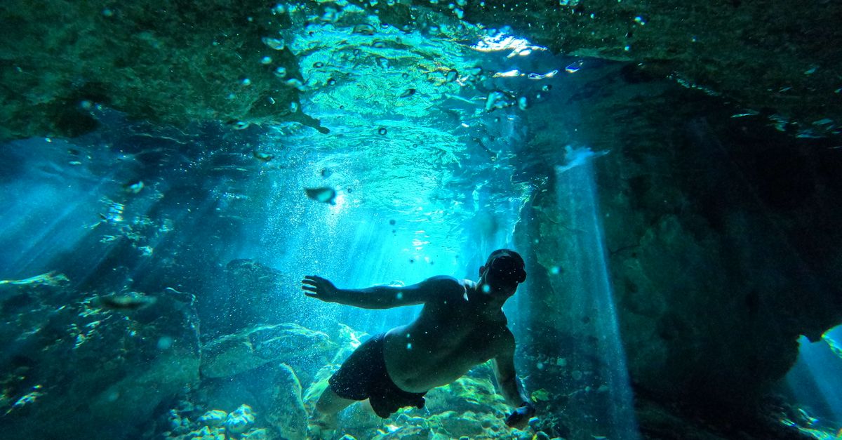 Diver at the bright entrance of an underwater cave in clear Maltese water.