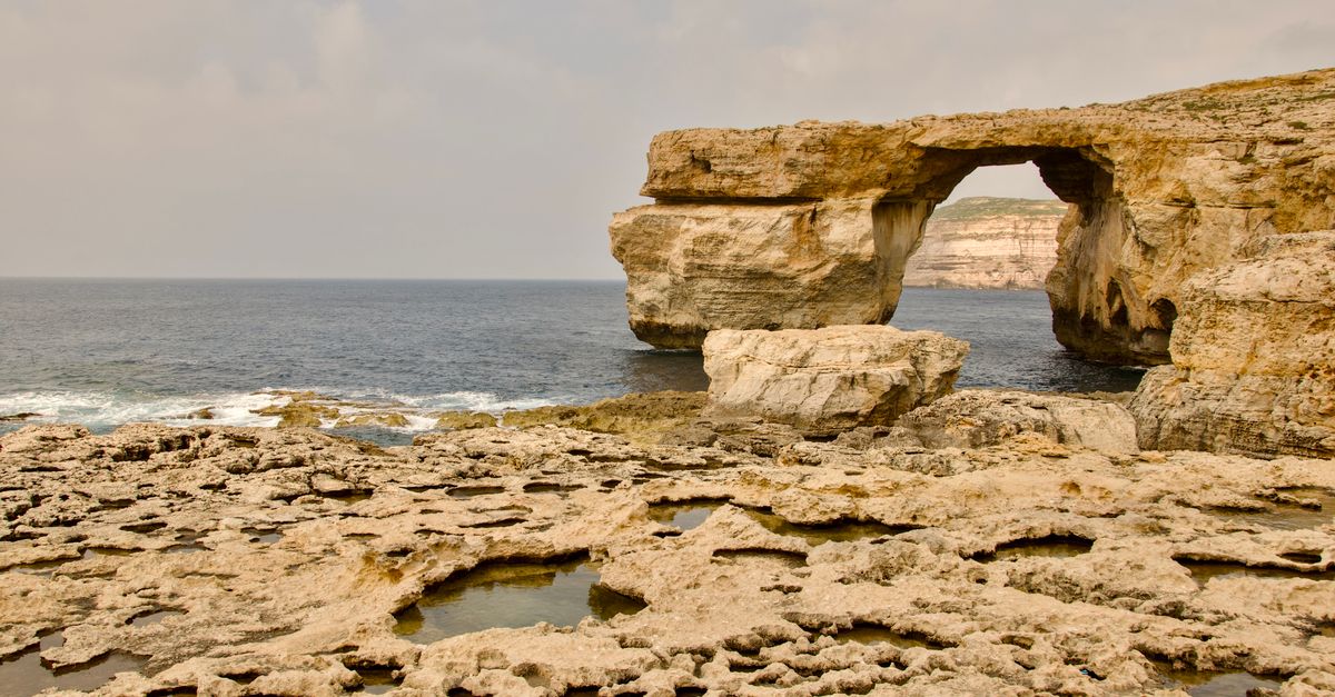 Limestone cliffs of a Maltese island rising above clear blue Mediterranean water.