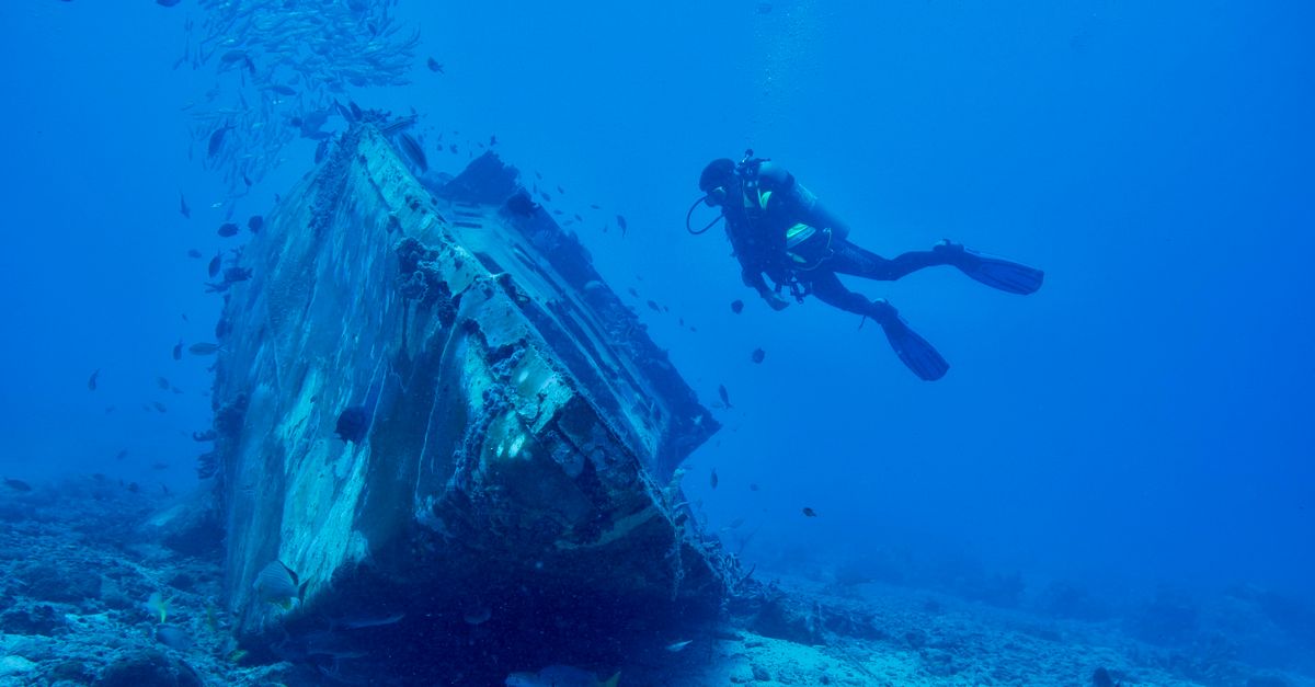 Dive boat with scuba equipment on deck anchored in calm blue Mediterranean water.